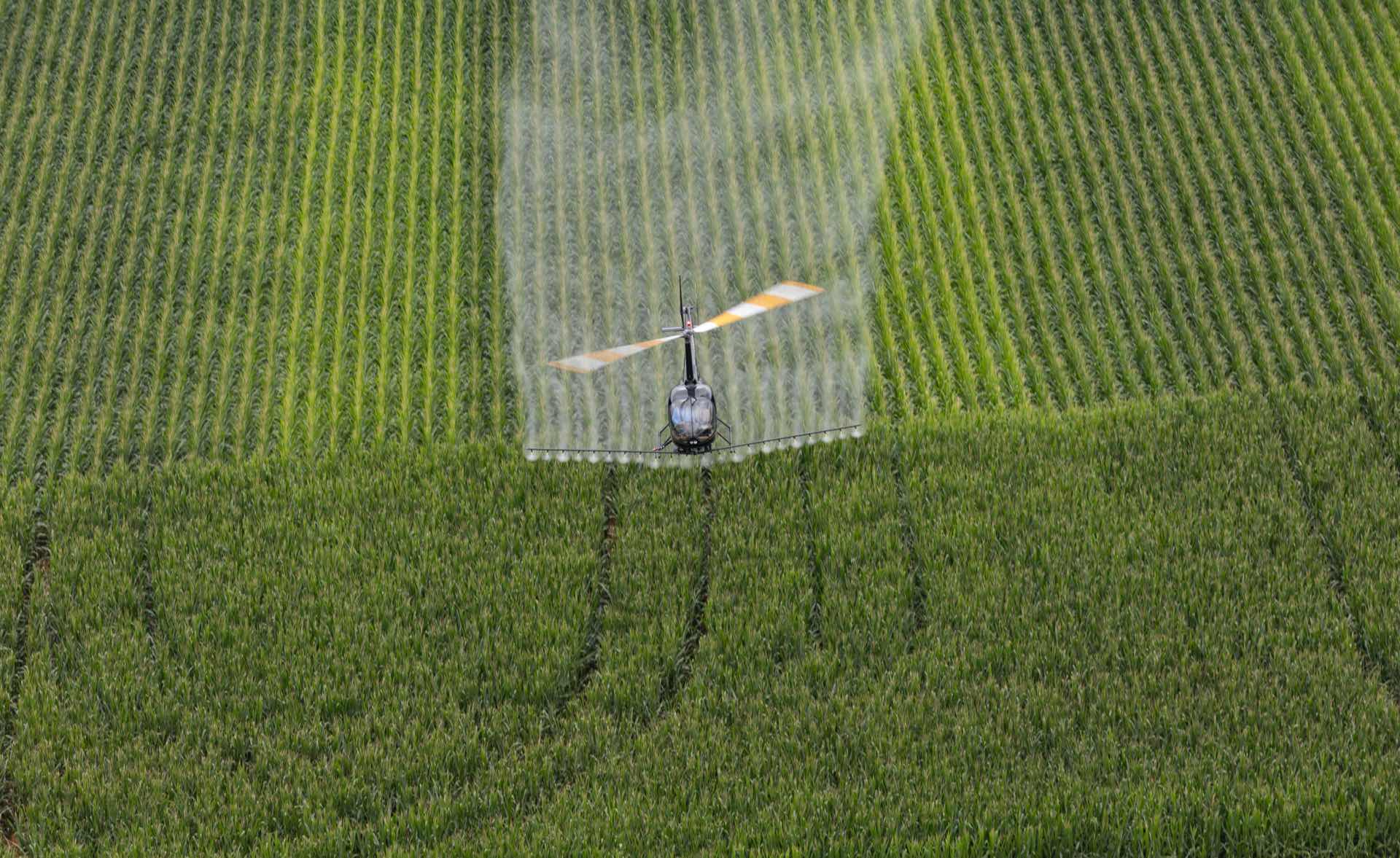 Robinson helicopter on an aerial application mission over row crops, spray boom deployed