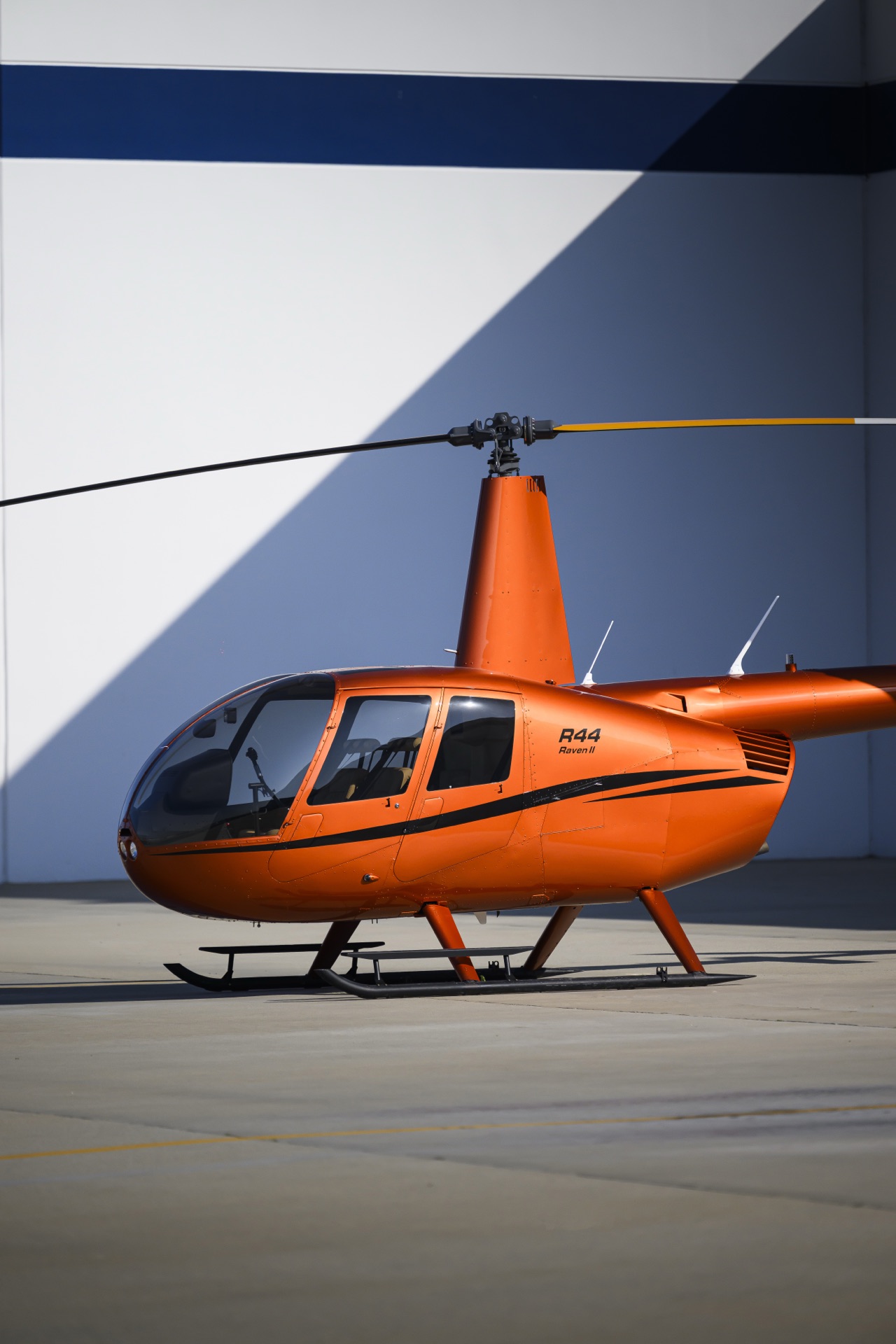 Orange Robinson R44 Raven II parked on the ramp outside a Robinson dealer hangar