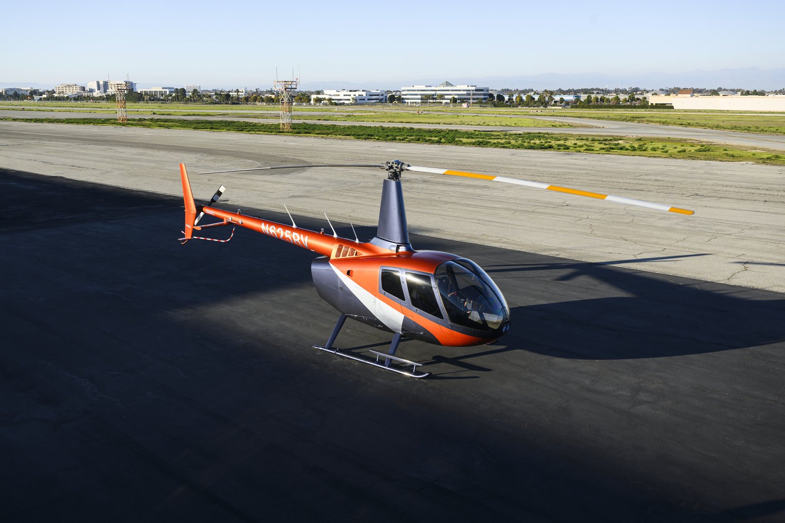 Orange Metallic Robinson R66 NxG with Bright Silver Metallic trim parked on the ramp, high-angle right-side view