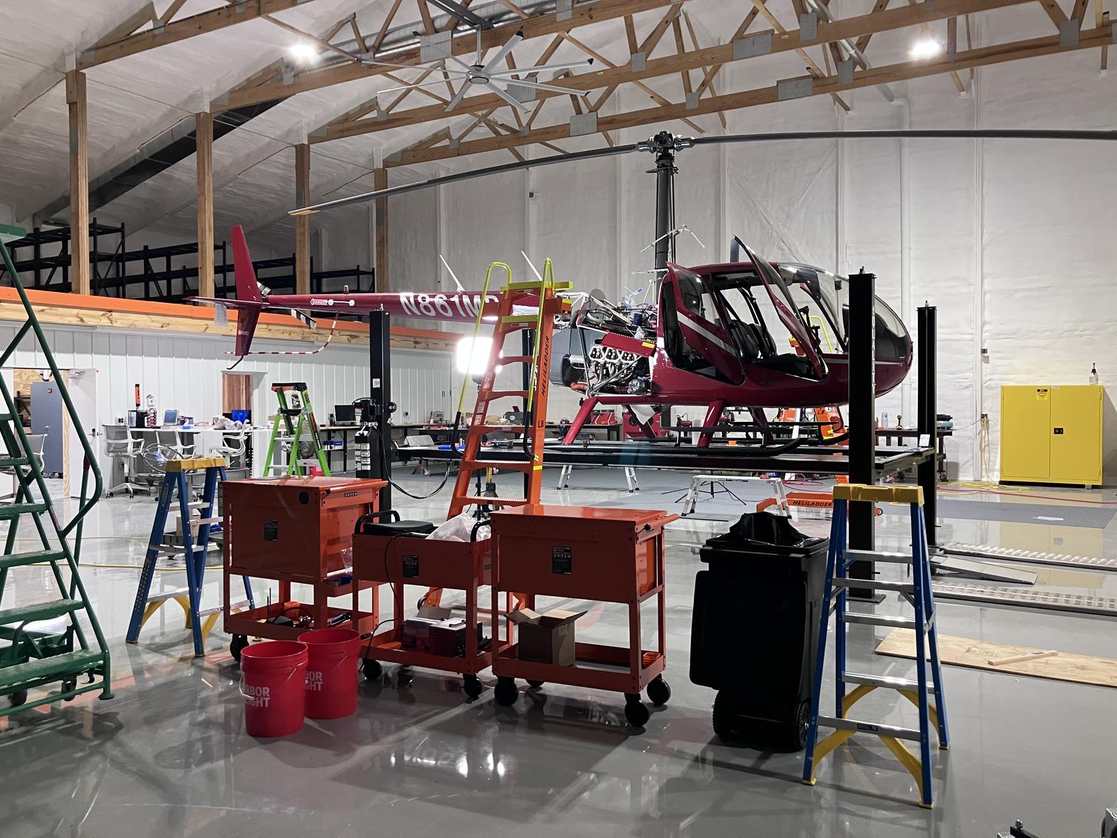 Robinson R44 raised on a maintenance lift in Castle's service bay with engine cowlings open